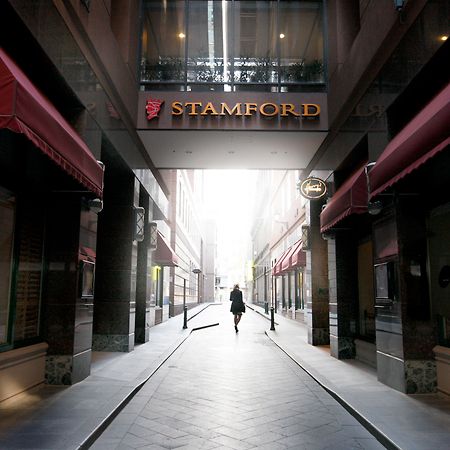 Stamford Plaza Melbourne Hotel Eksteriør billede The photo depicts a narrow alley or passageway, possibly in an urban setting. On one side, there are storefronts with canopies, and on the opposite side, there is a prominent sign reading "STAMFORD." The pathway is lined with buildings, creating a se