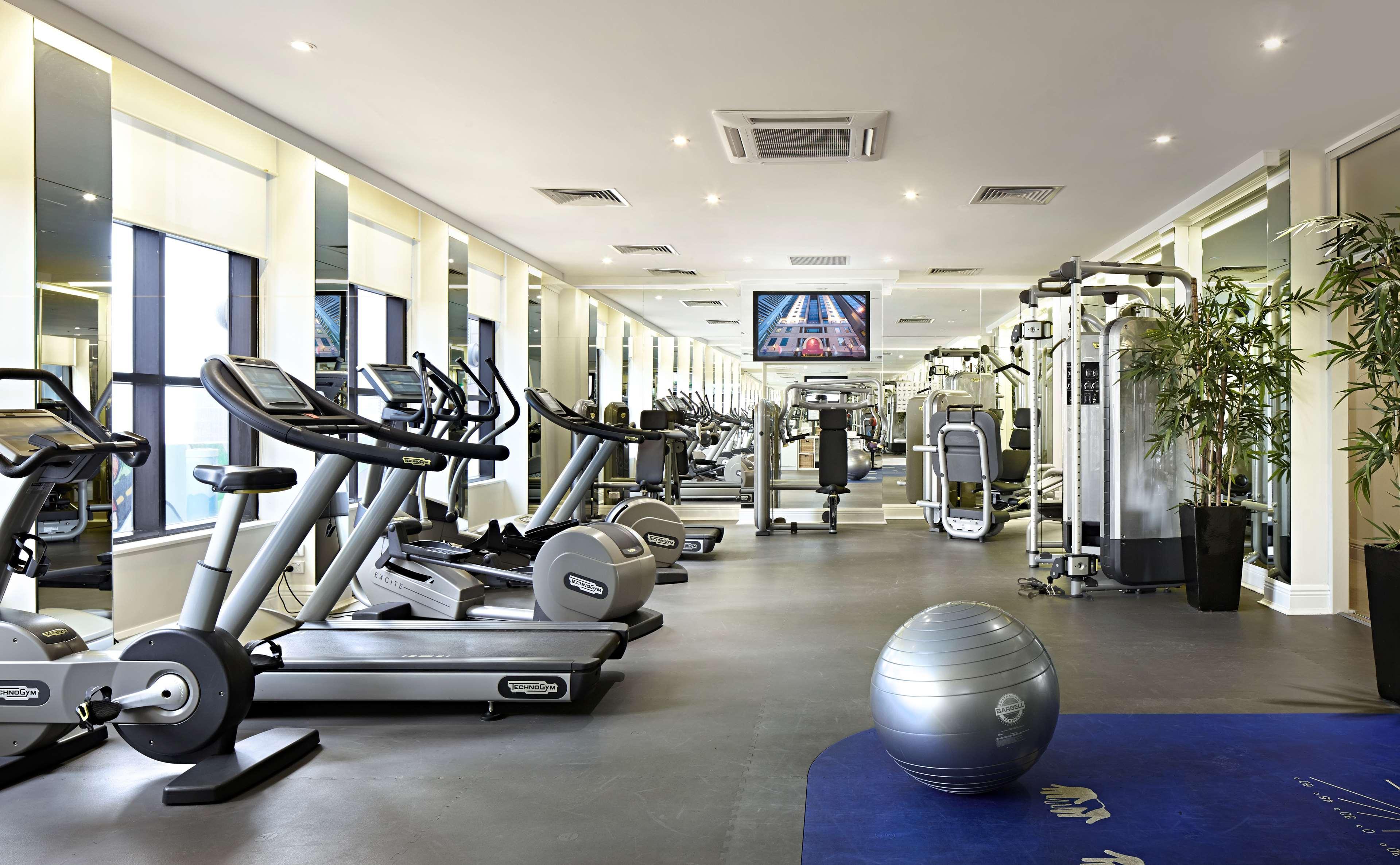 Stamford Plaza Melbourne Hotel Eksteriør billede The photo shows a modern gym or fitness center. There are several exercise machines, including treadmills and elliptical trainers, positioned near large windows that allow natural light to flood the space. A television is mounted on the wall, likely 