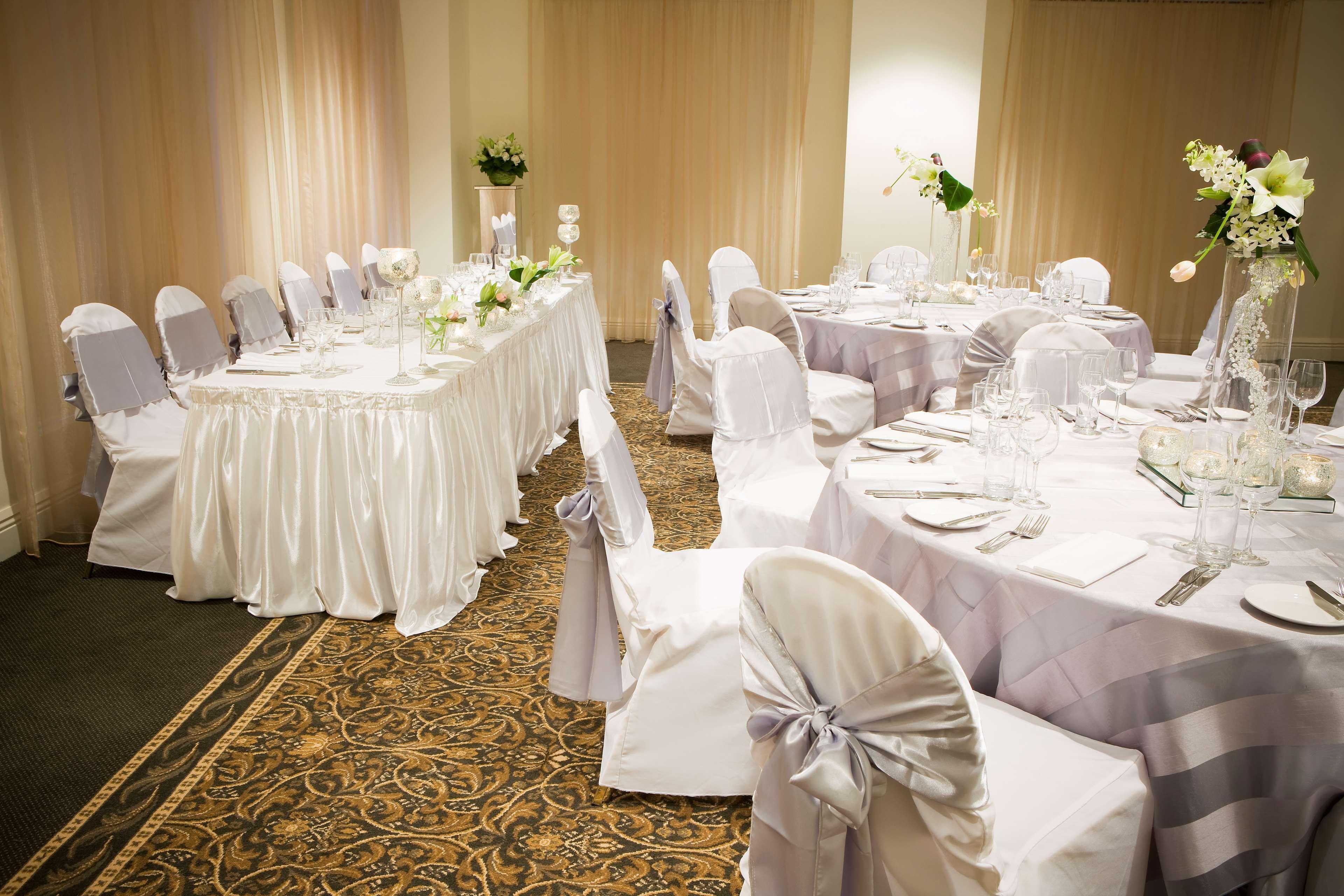 Stamford Plaza Melbourne Hotel Eksteriør billede The photo depicts an elegantly set dining area, likely for a special event or celebration. There are several round tables covered with tablecloths, each set with plates, glassware, and cutlery. The chairs are dressed in white covers, some adorned wit