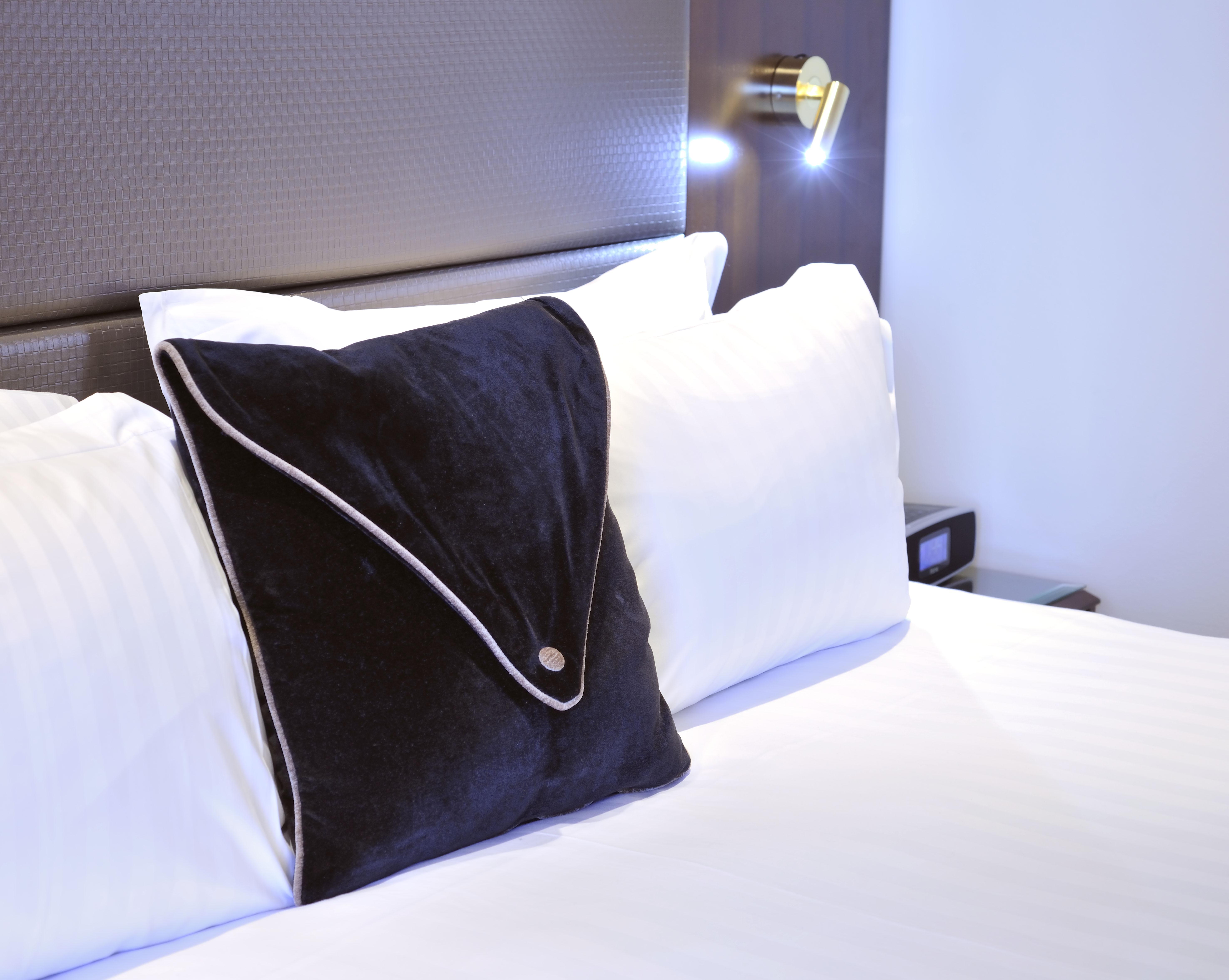 Stamford Plaza Melbourne Hotel Eksteriør billede The photo shows a neatly arranged bed with white linens. There are several pillows, with one black pillow featuring a distinctive design on top of the white pillows. The headboard of the bed is visible, along with a stylish wall-mounted light fixture