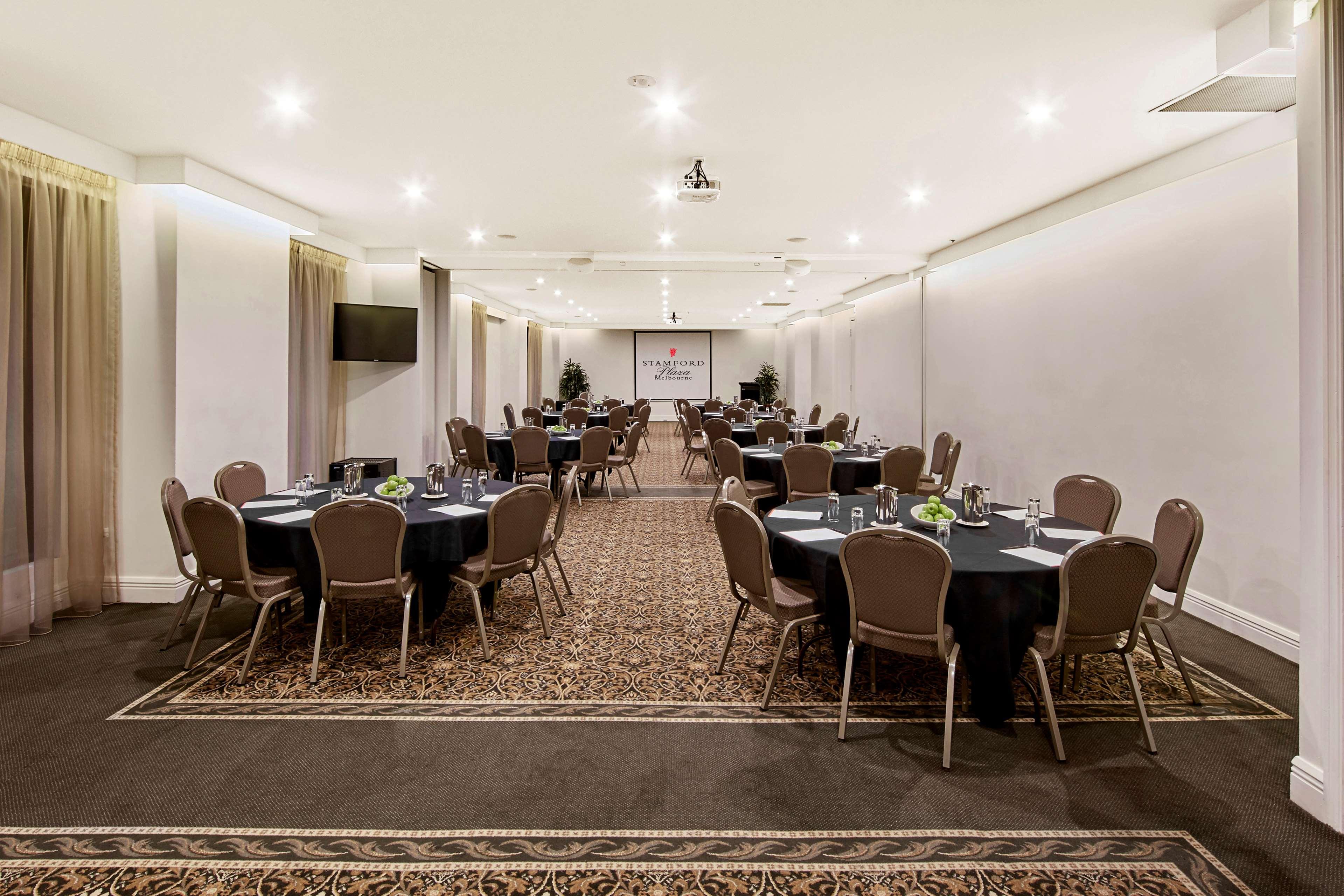 Stamford Plaza Melbourne Hotel Eksteriør billede The photo shows an event space or banquet hall set up for a gathering. The room features several round tables covered with black tablecloths, each adorned with small centerpieces. Chairs are arranged around each table. The lighting is bright and mode