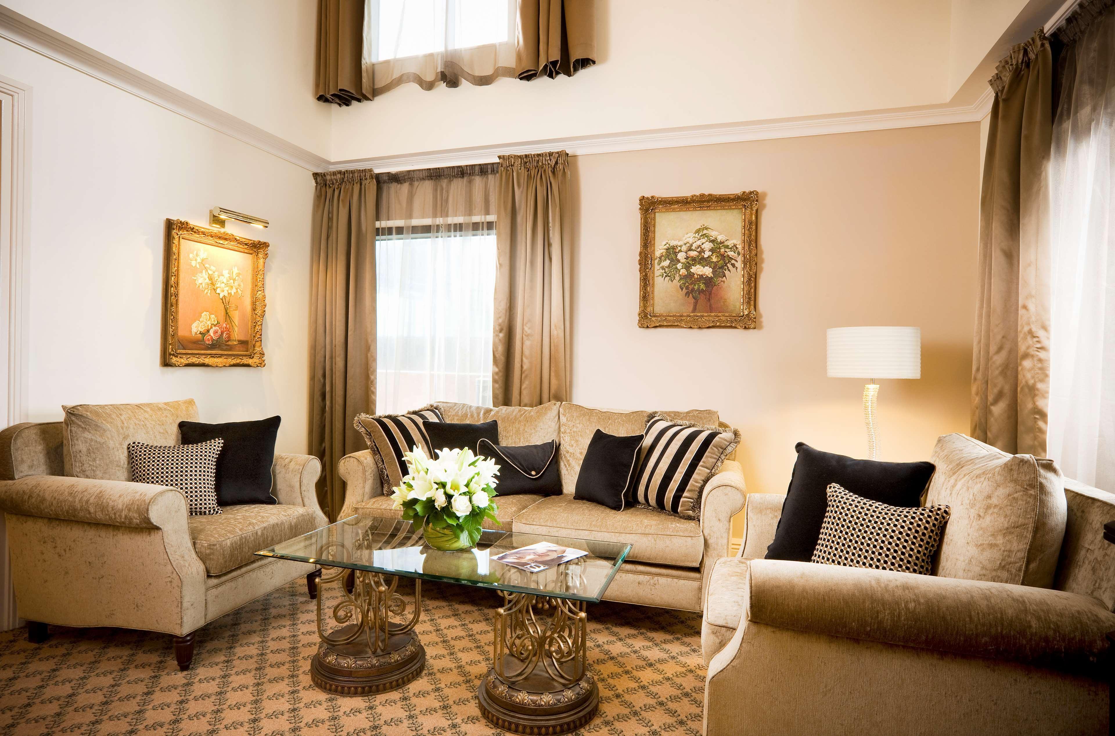 Stamford Plaza Melbourne Hotel Værelse billede The photo depicts a stylish living room with a warm and inviting aesthetic. It features a set of comfortable beige sofas adorned with decorative pillows in black and patterned designs. There is a glass coffee table at the center, supported by elegant