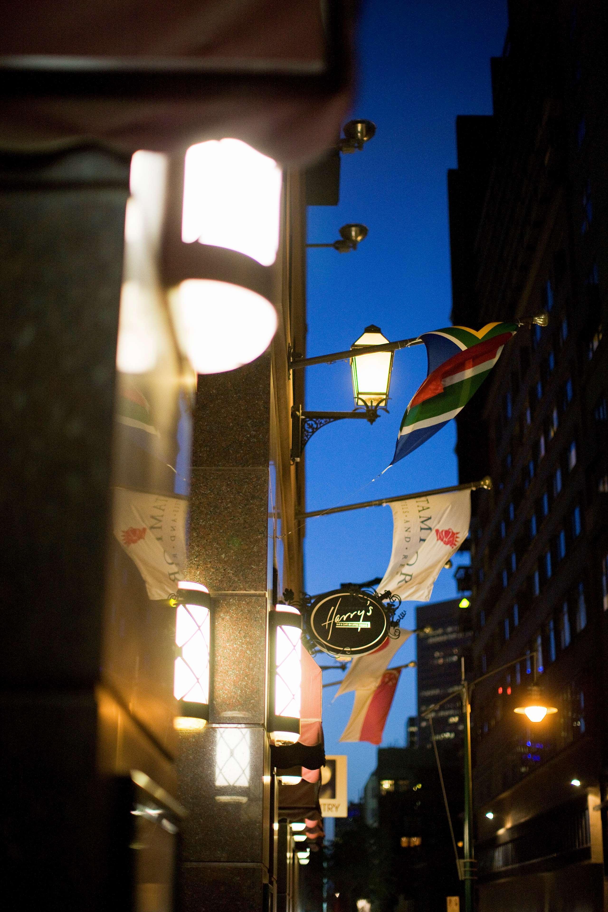 Stamford Plaza Melbourne Hotel Eksteriør billede The photo features a street view of a building at dusk. Prominently displayed are several flags, including a South African flag, which are fluttering in the wind. There is a sign that reads "Harry's," likely indicating the name of a business or estab
