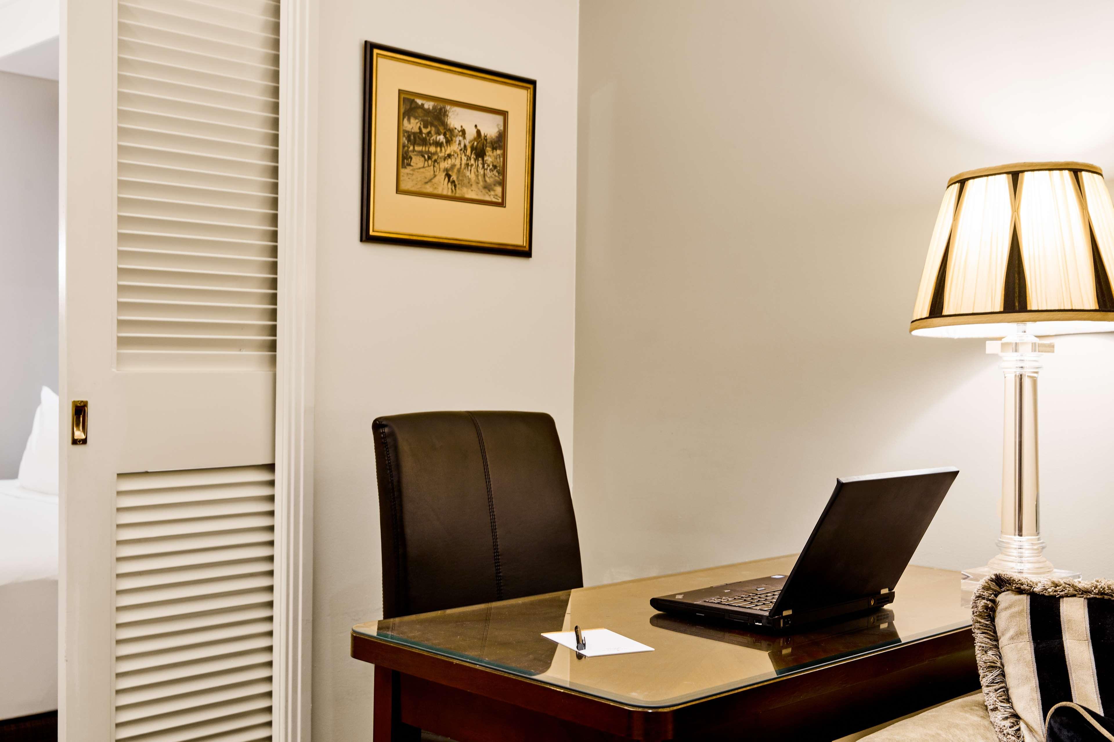 Stamford Plaza Melbourne Hotel Eksteriør billede The photo shows a small office or workspace. There is a desk with a glass surface, and on it sits a laptop computer. A piece of paper or notecard is also placed on the desk. Behind the desk is a black office chair. A wall lamp with a striped shade is