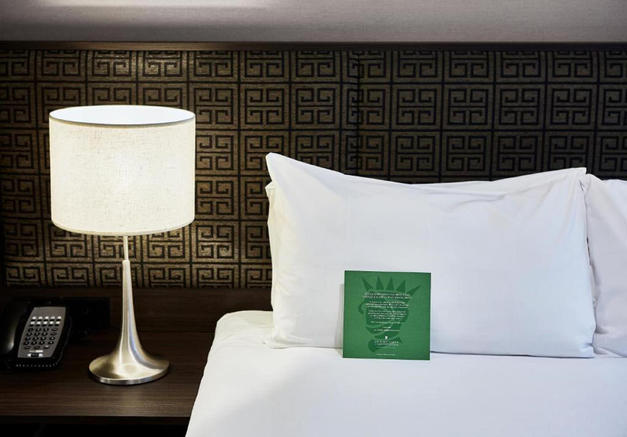 Stamford Plaza Melbourne Hotel Eksteriør billede The photo shows a neatly made bed with a white pillow and a green item placed on top of it. Next to the bed, there is a stylish table lamp with a lampshade that appears to be white. In the background, you can see a patterned wall, which has a geometr