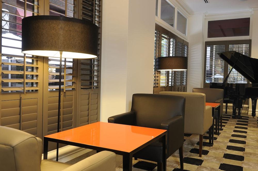 Stamford Plaza Melbourne Hotel Eksteriør billede The photo shows a cozy interior space, likely a lounge or café. It features a modern design with a mix of seating options, including black and light-colored chairs surrounding small tables. One table has a bright orange top, creating a striking visua