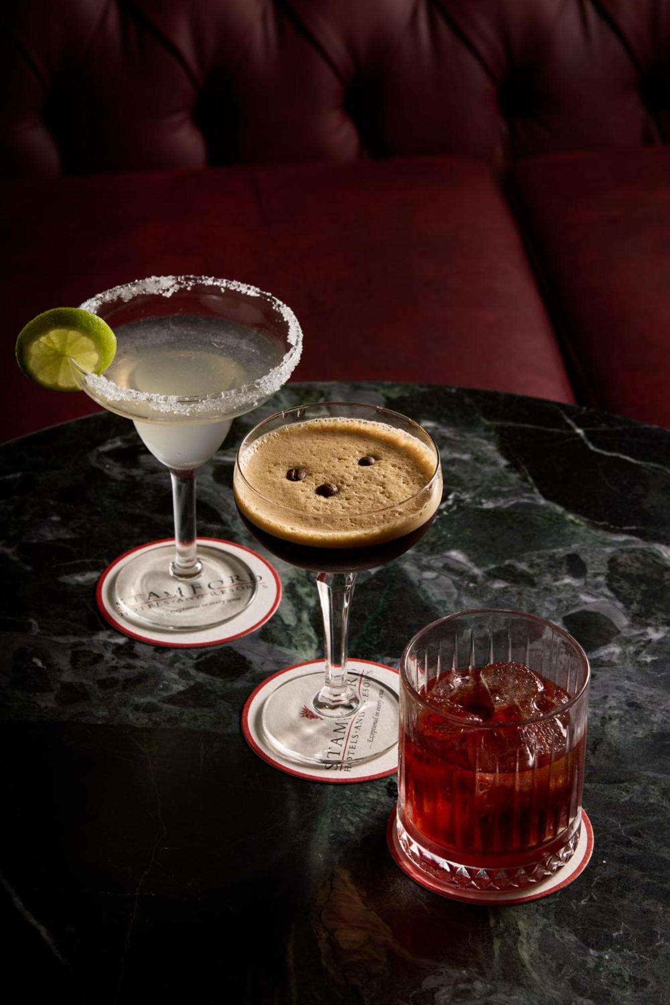 Stamford Plaza Melbourne Hotel Eksteriør billede The photo displays three different cocktails arranged on a dark marble table. 

1. On the left, there is a margarita glass filled with a clear drink, garnished with a lime slice and featuring a salted rim.
2. In the center, a coupe glass holds a dark