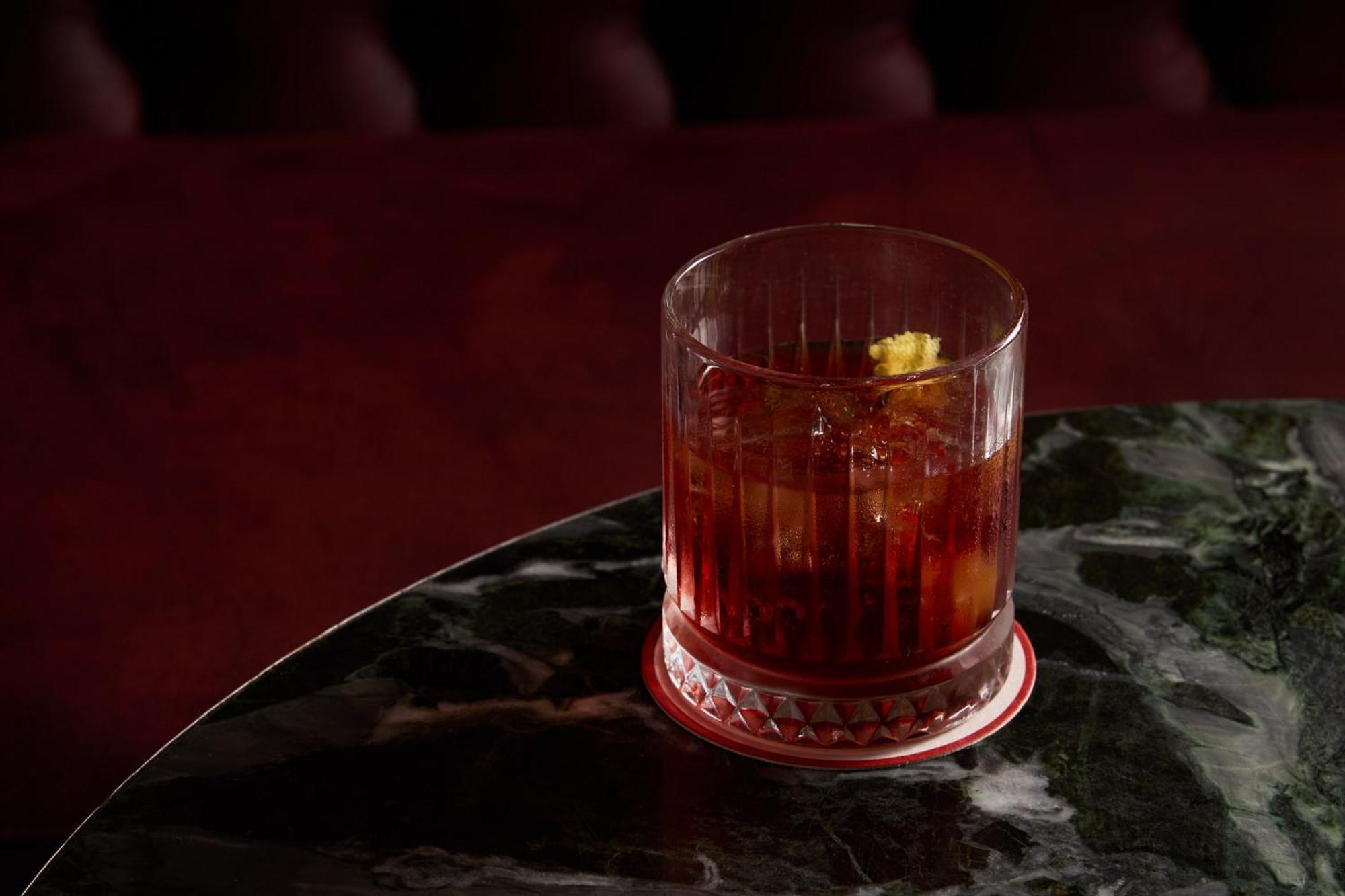 Stamford Plaza Melbourne Hotel Eksteriør billede The photo depicts a short glass filled with a dark-colored beverage, likely an alcoholic drink. The glass has a textured design, with ice cubes visible inside. A twist of lemon peel is perched on the rim, adding a touch of garnish. The drink sits on 