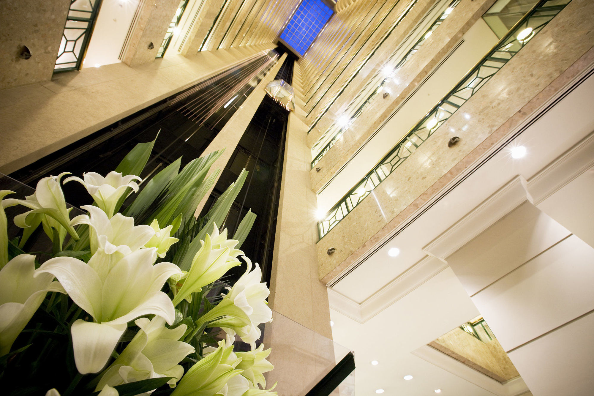 Stamford Plaza Melbourne Hotel Interiør billede The photo shows a modern indoor space, likely a lobby or atrium of a building. The view is looking upwards, capturing a sleek design with multiple levels. There are several elevators in the center, running vertically. The walls are lined with glass a